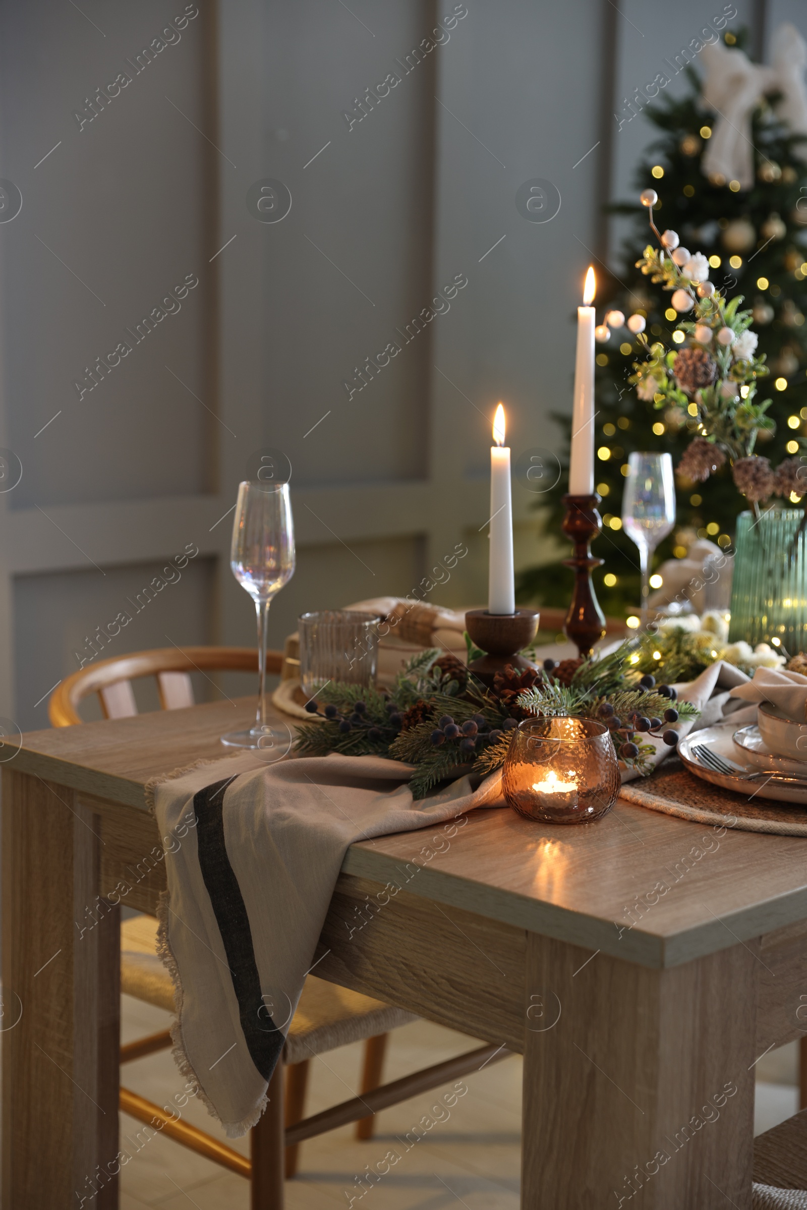 Photo of Christmas table setting with stylish dishware, glasses and burning candles in festive decorated room