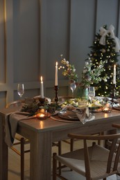 Photo of Christmas table setting with stylish dishware, glasses and burning candles in festive decorated room