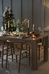 Photo of Christmas table setting with stylish dishware, glasses and burning candles in festive decorated room