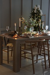 Photo of Christmas table setting with stylish dishware, glasses and burning candles in festive decorated room