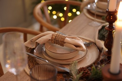 Photo of Christmas place setting with festive decor on wooden table in room, closeup