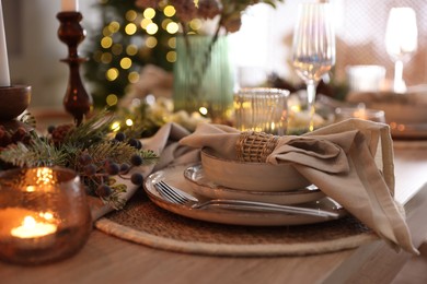 Photo of Christmas place setting with festive decor on wooden table in room, closeup