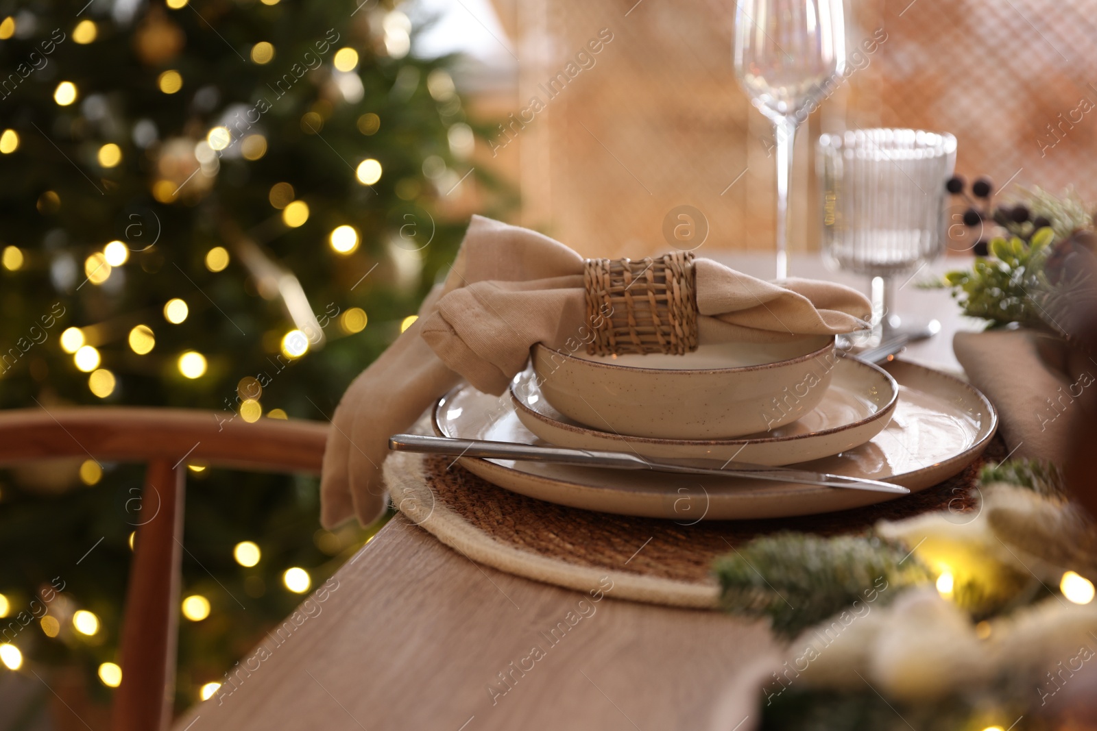 Photo of Christmas celebration. Festive table setting with dishware, glasses and decor in room, closeup