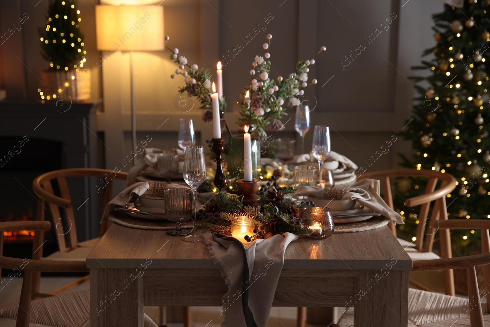 Photo of Christmas table setting with stylish dishware, glasses and burning candles in festive decorated room