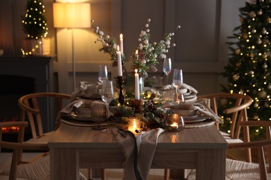 Photo of Christmas table setting with stylish dishware, glasses and burning candles in festive decorated room