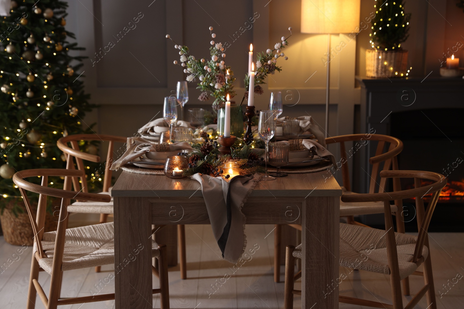 Photo of Christmas table setting with stylish dishware, glasses and burning candles in festive decorated room