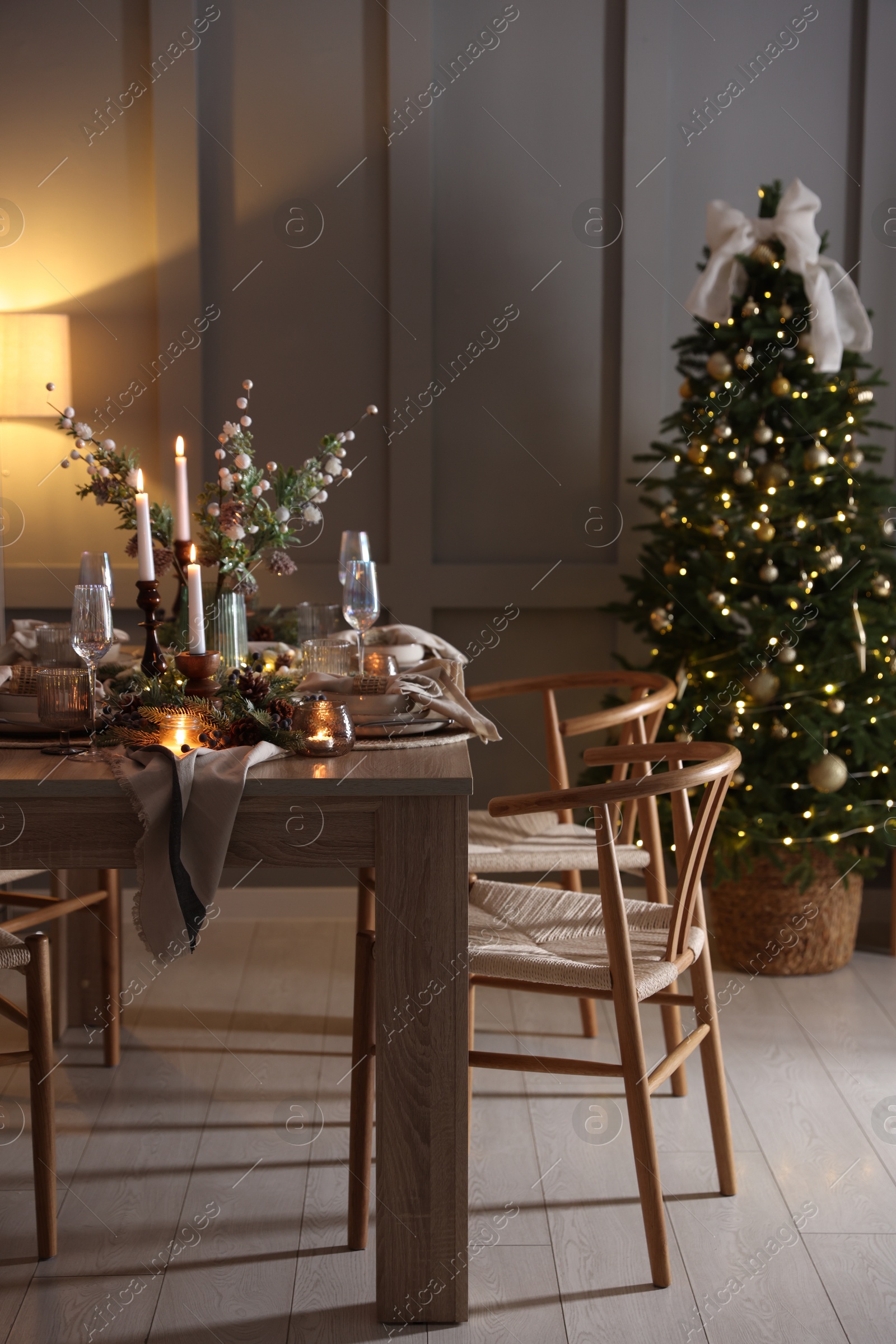 Photo of Christmas table setting with stylish dishware, glasses and burning candles in festive decorated room