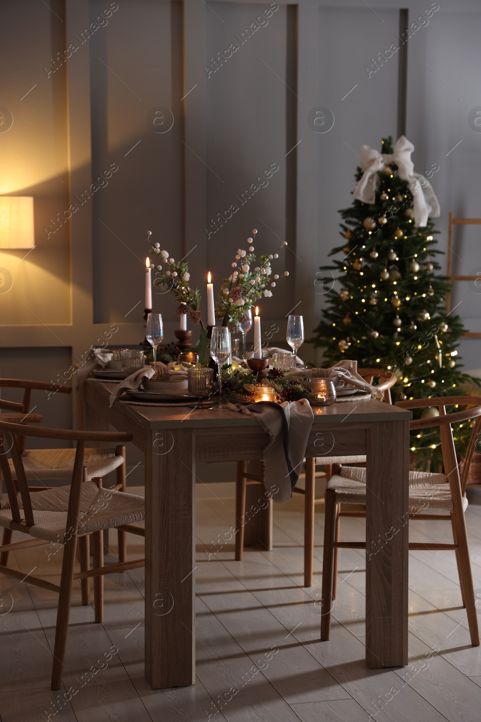 Photo of Christmas table setting with stylish dishware, glasses and burning candles in festive decorated room