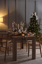 Photo of Christmas table setting with stylish dishware, glasses and burning candles in festive decorated room