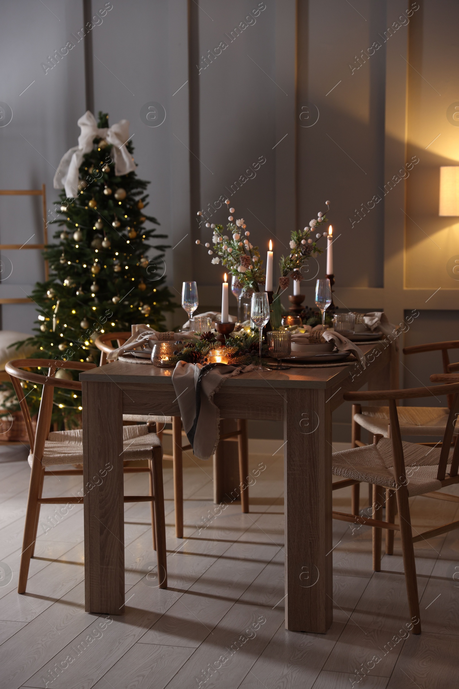 Photo of Christmas table setting with stylish dishware, glasses and burning candles in festive decorated room