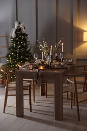 Photo of Christmas table setting with stylish dishware, glasses and burning candles in festive decorated room