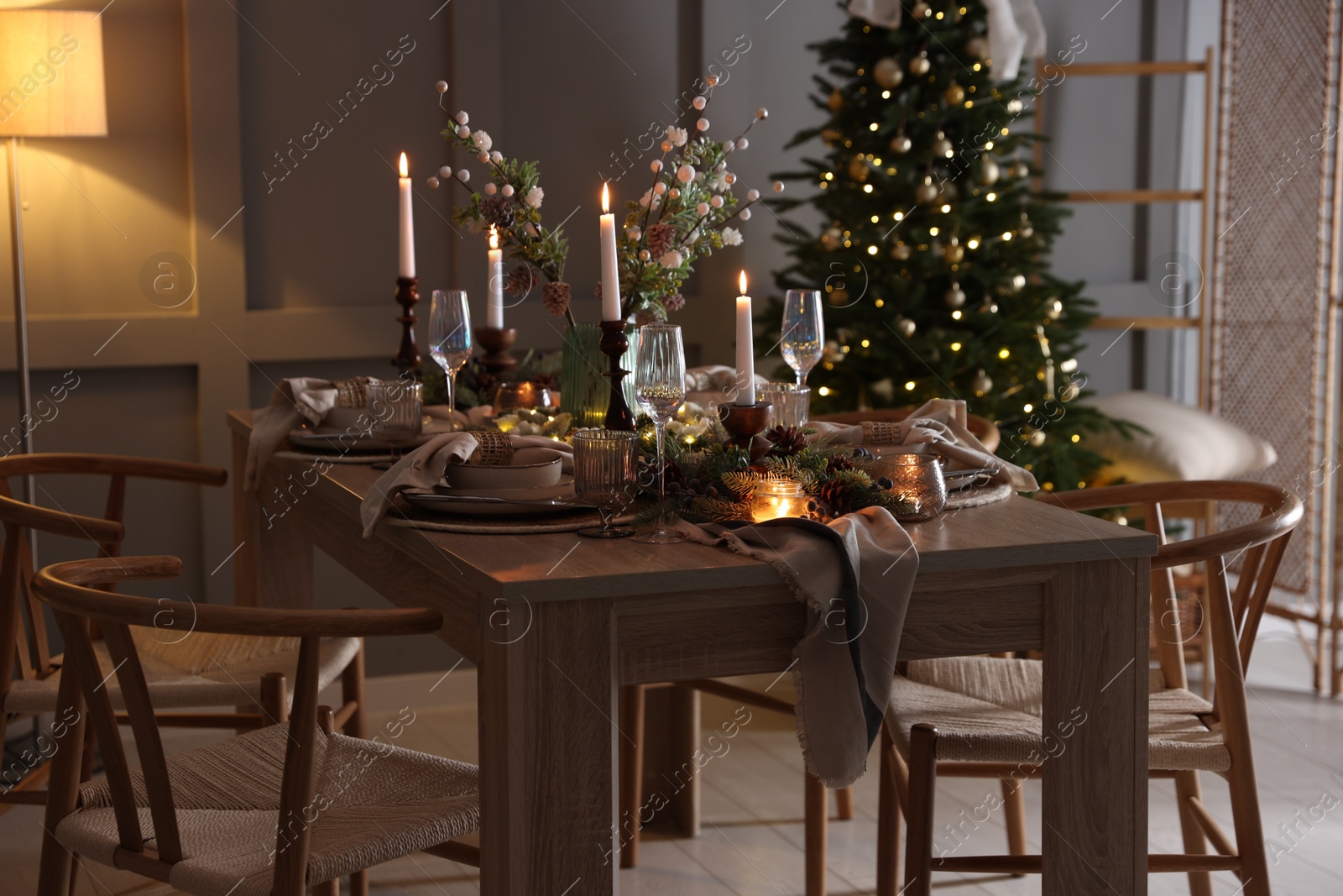 Photo of Christmas table setting with stylish dishware, glasses and burning candles in festive decorated room