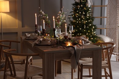 Photo of Christmas table setting with stylish dishware, glasses and burning candles in festive decorated room