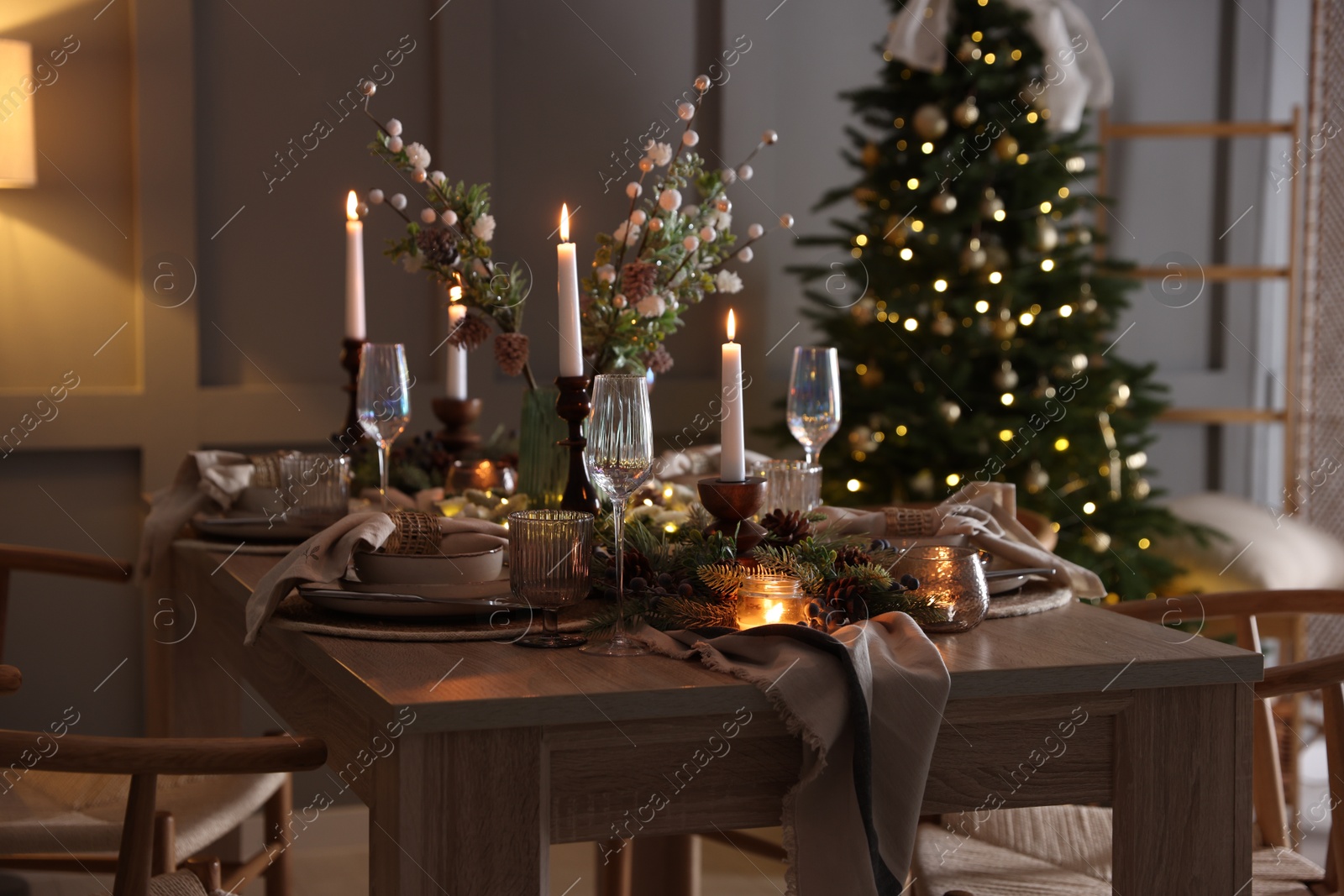 Photo of Christmas table setting with stylish dishware, glasses and burning candles in festive decorated room