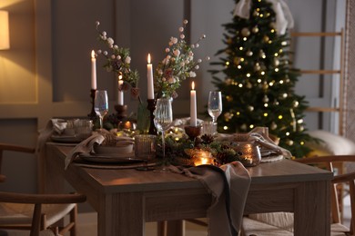 Photo of Christmas table setting with stylish dishware, glasses and burning candles in festive decorated room