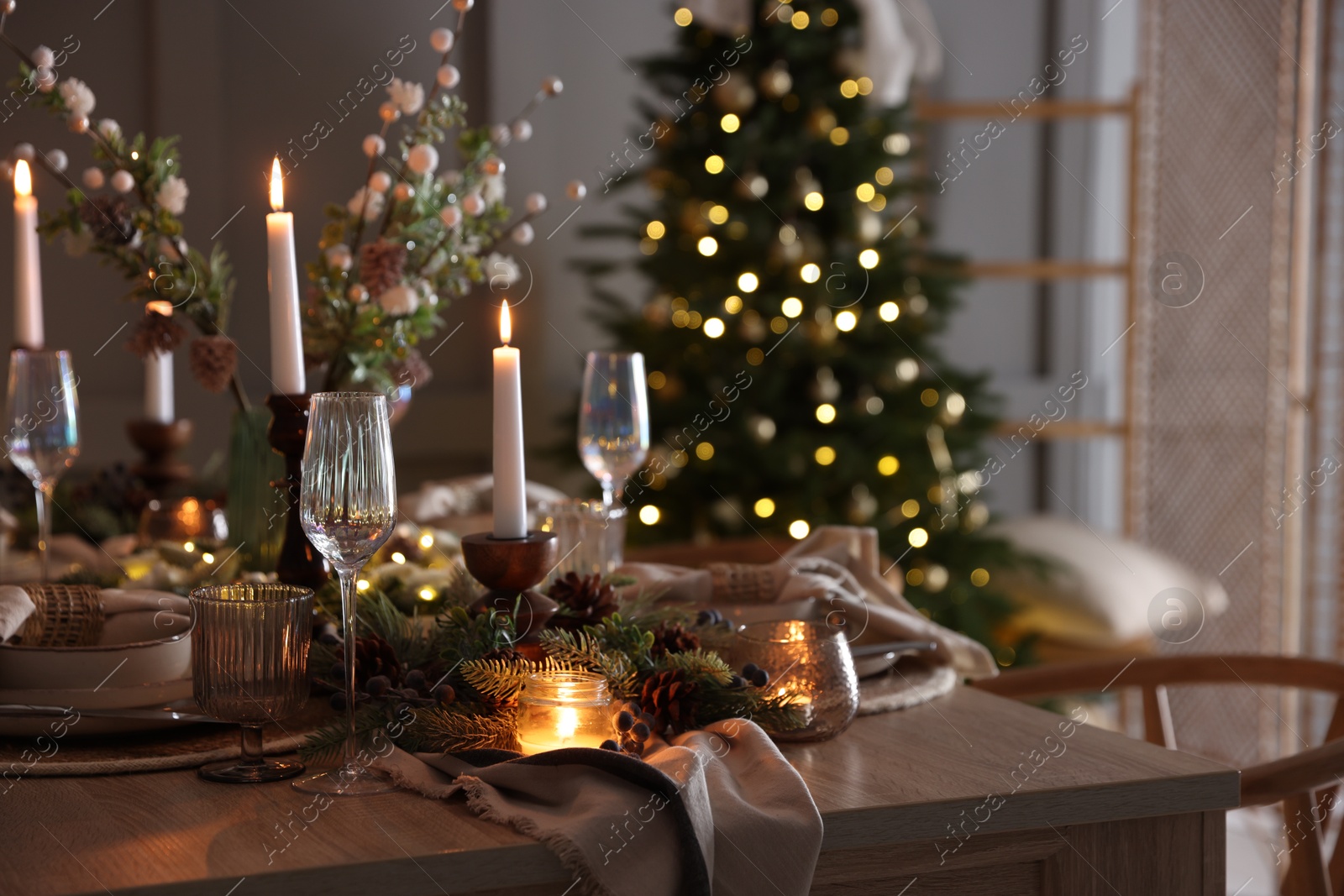 Photo of Christmas table setting with stylish dishware, glasses and burning candles in festive decorated room