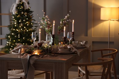 Photo of Christmas table setting with stylish dishware, glasses and burning candles in festive decorated room