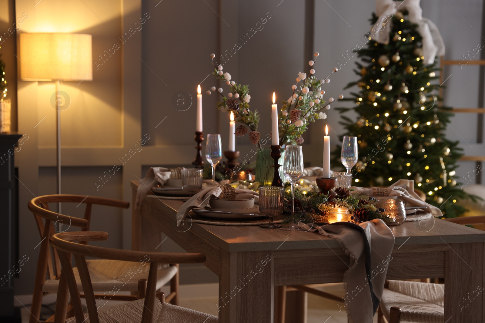 Photo of Christmas table setting with stylish dishware, glasses and burning candles in festive decorated room