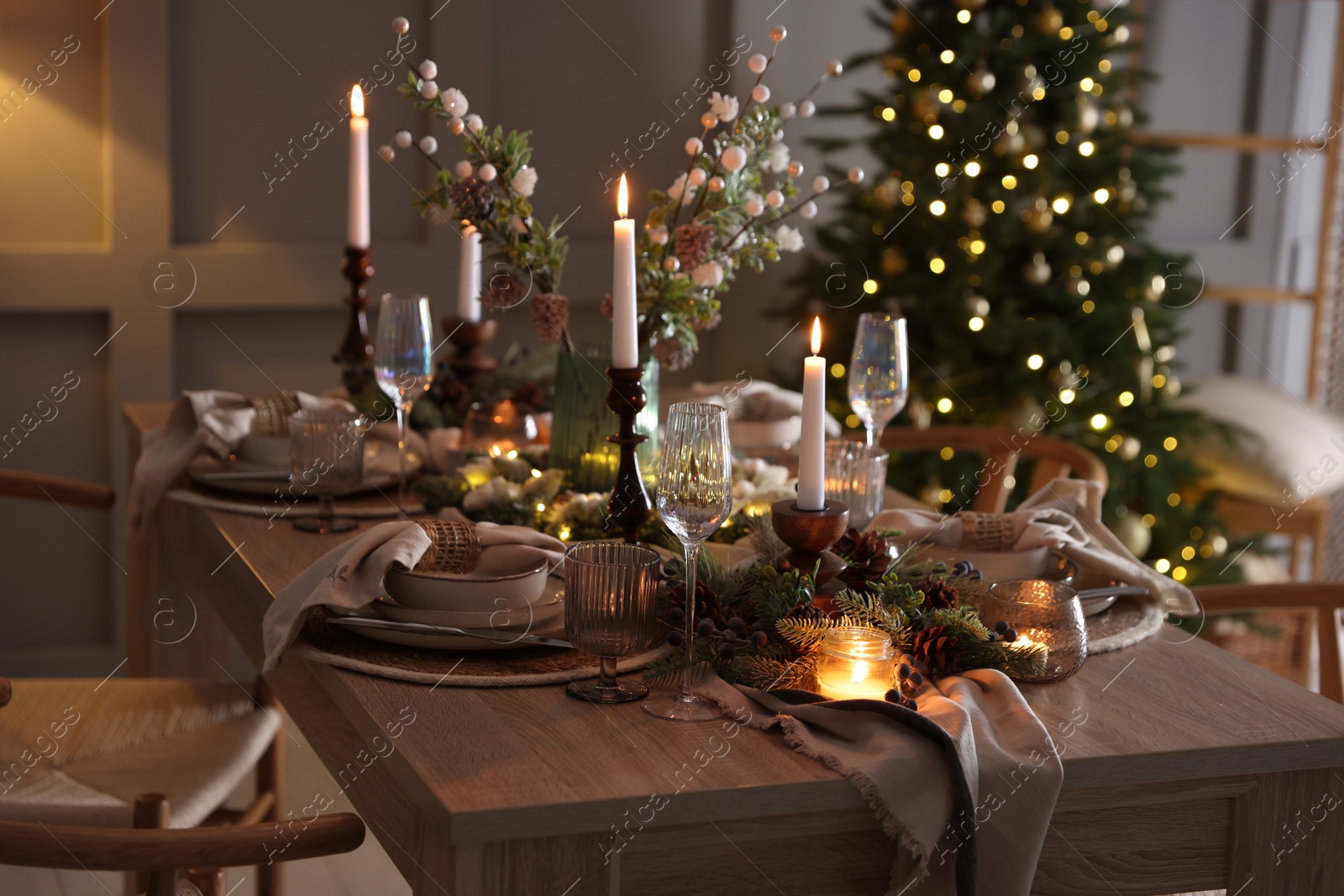 Photo of Christmas table setting with stylish dishware, glasses and burning candles in festive decorated room