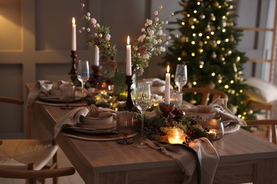 Photo of Christmas table setting with stylish dishware, glasses and burning candles in festive decorated room