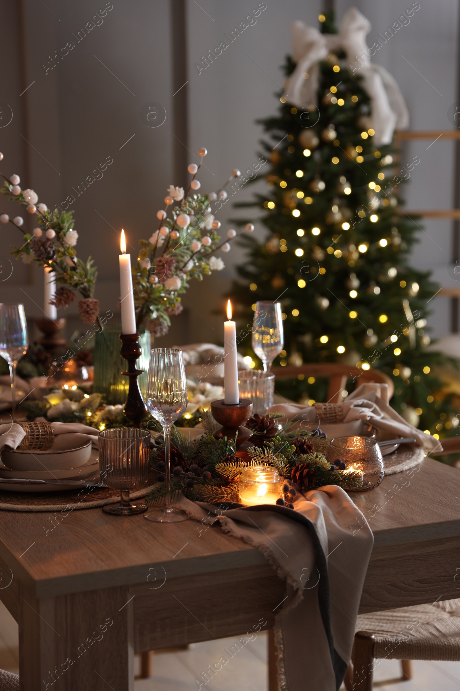 Photo of Christmas table setting with stylish dishware, glasses and burning candles in festive decorated room