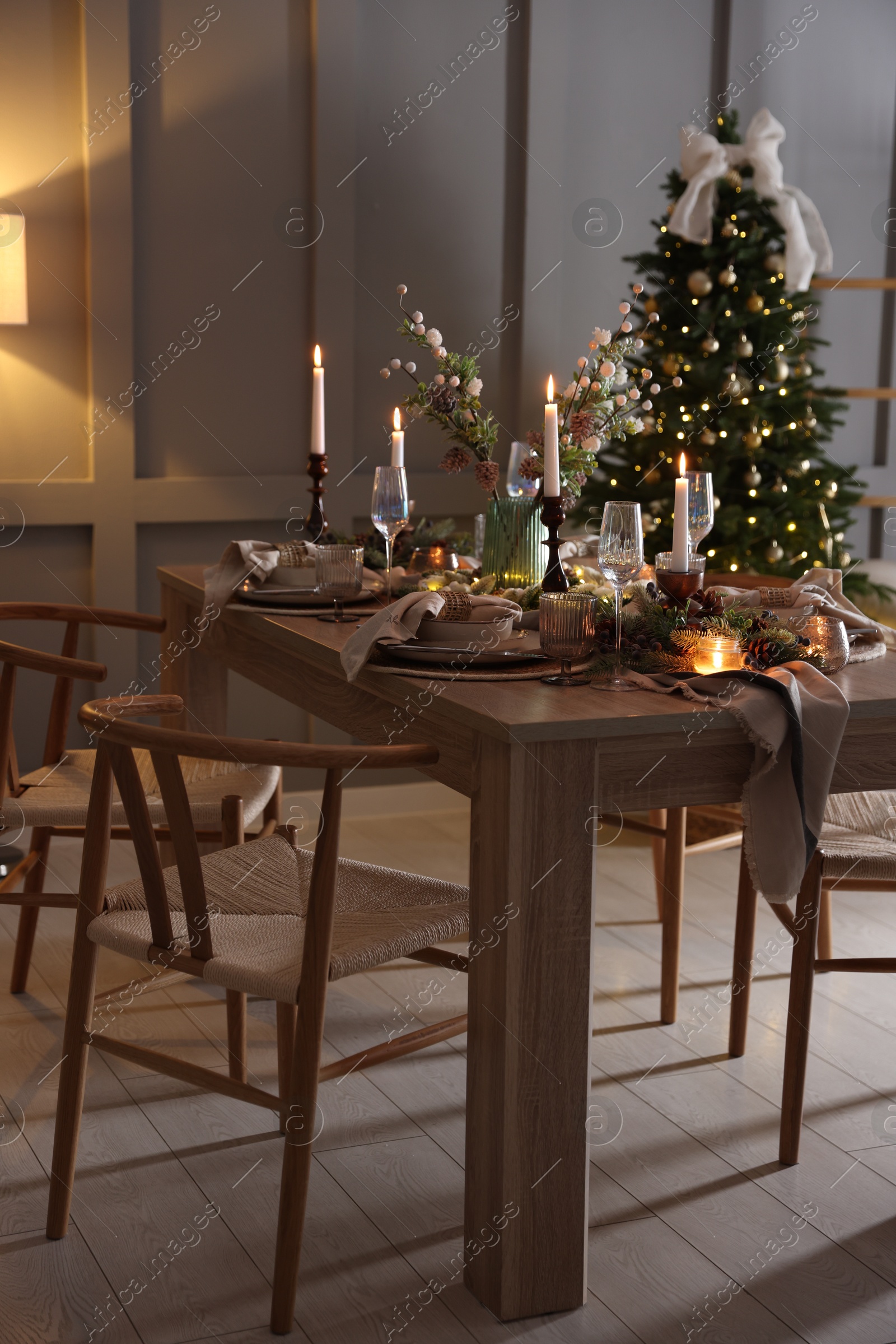 Photo of Christmas table setting with stylish dishware, glasses and burning candles in festive decorated room