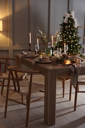 Photo of Christmas table setting with stylish dishware, glasses and burning candles in festive decorated room