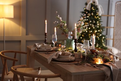 Photo of Christmas table setting with stylish dishware, glasses and burning candles in festive decorated room