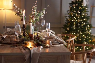 Photo of Christmas table setting with stylish dishware, glasses and burning candles in festive decorated room