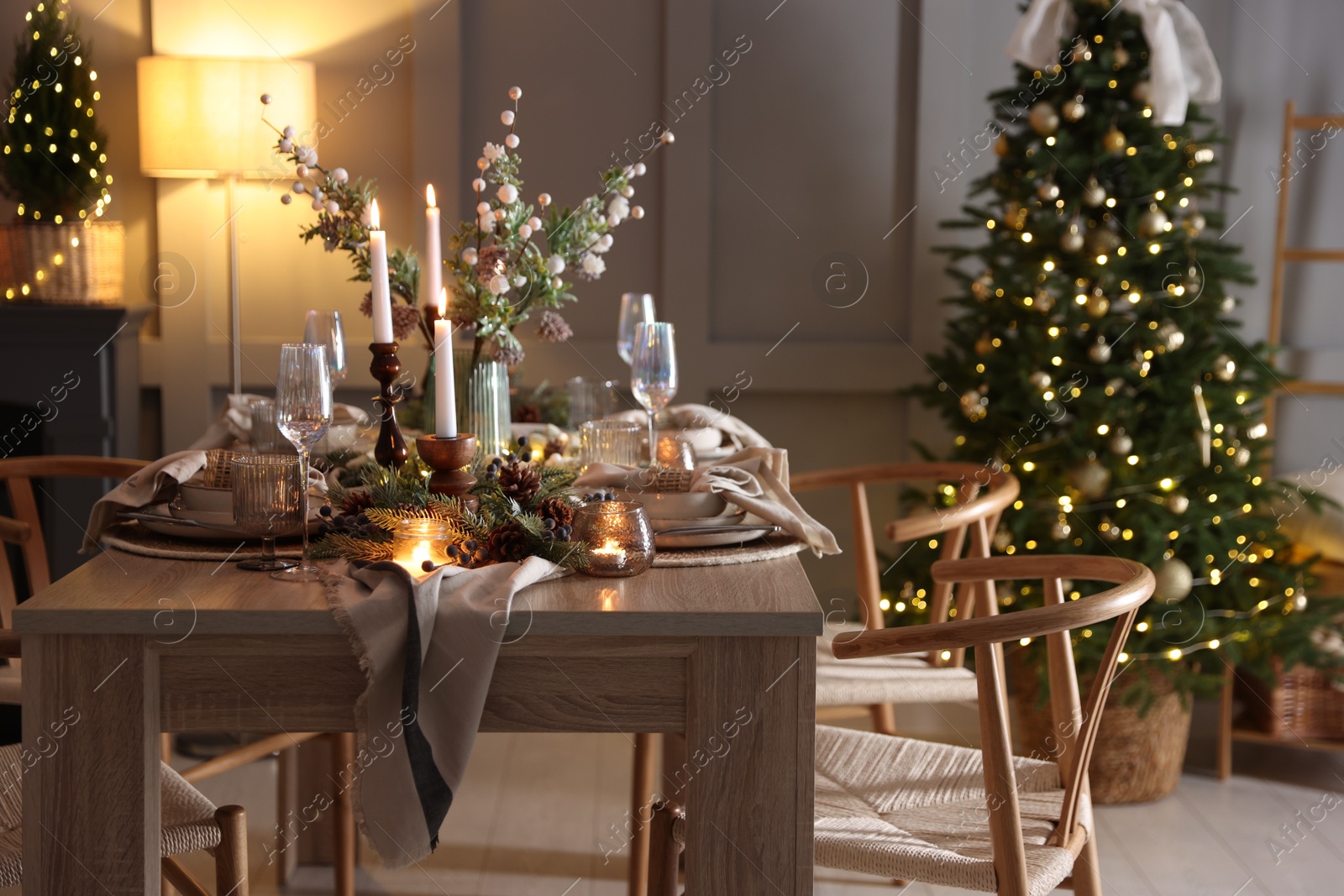 Photo of Christmas table setting with stylish dishware, glasses and burning candles in festive decorated room