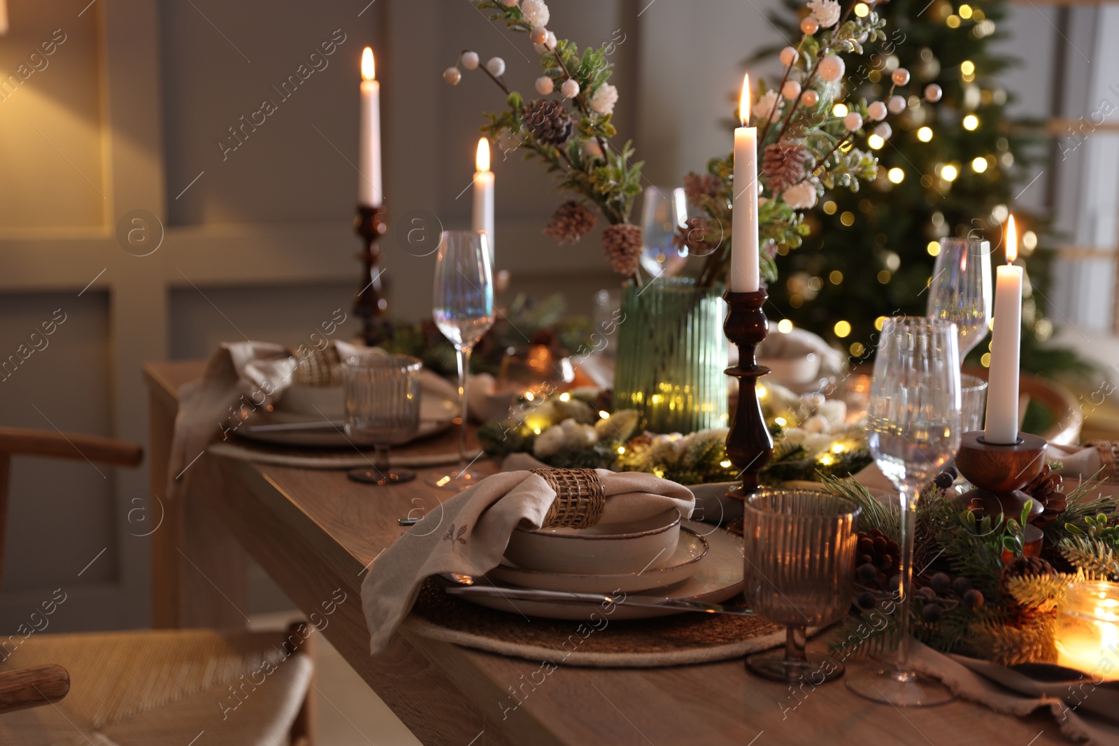 Photo of Christmas table setting with stylish dishware, glasses and burning candles in festive decorated room