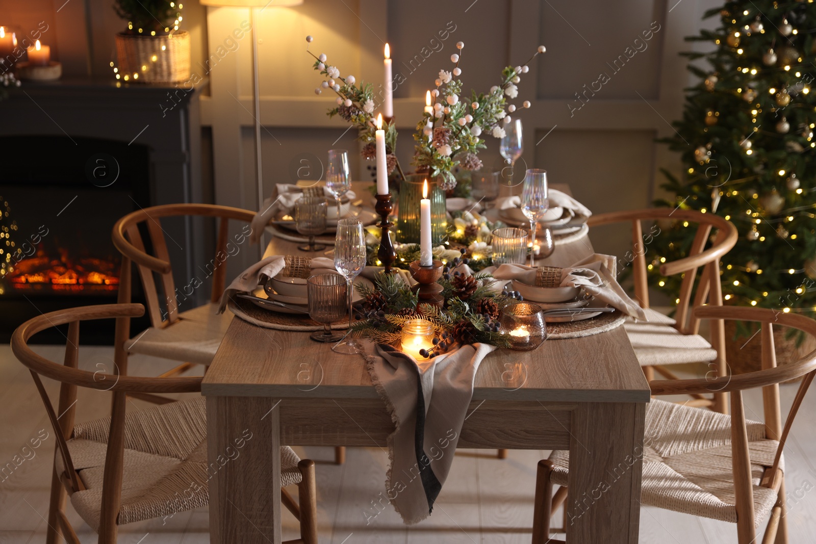 Photo of Christmas table setting with stylish dishware, glasses and burning candles in festive decorated room