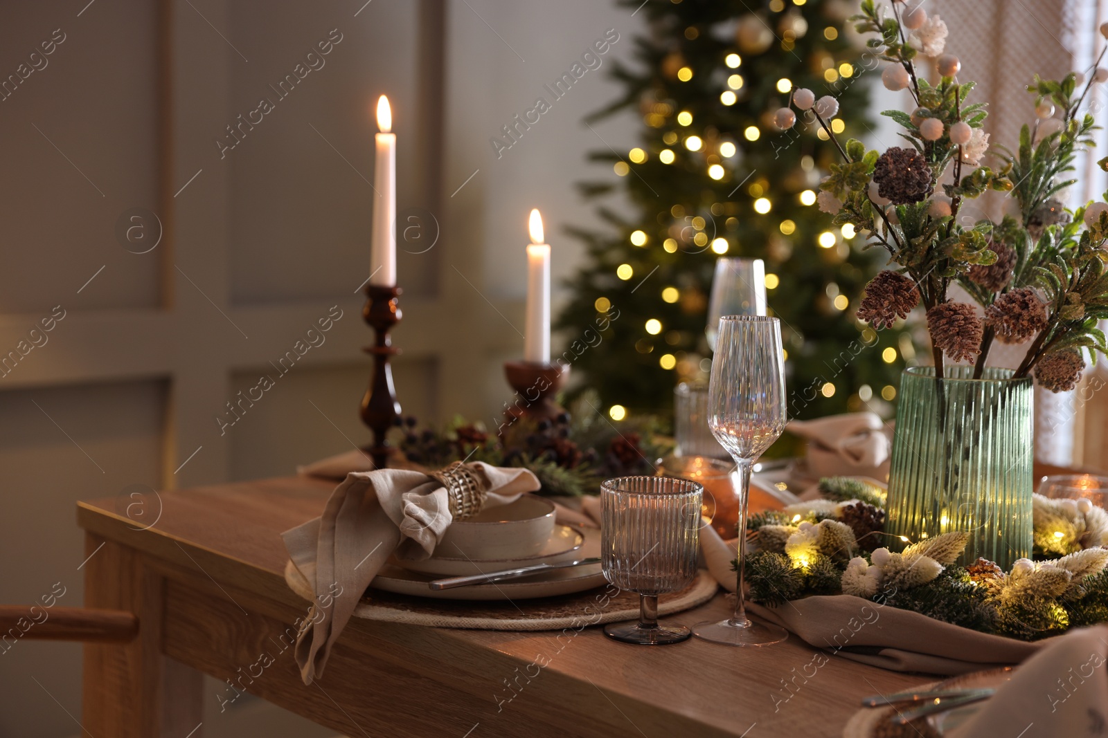 Photo of Christmas table setting with stylish dishware, glasses and burning candles in festive decorated room