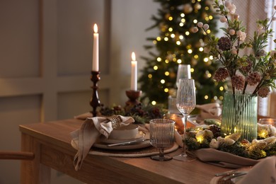 Photo of Christmas table setting with stylish dishware, glasses and burning candles in festive decorated room