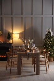 Photo of Christmas table setting with stylish dishware, glasses and burning candles in festive decorated room