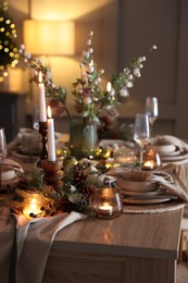 Photo of Christmas table setting with stylish dishware, glasses and burning candles in festive decorated room