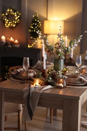 Photo of Christmas table setting with stylish dishware, glasses and burning candles in festive decorated room