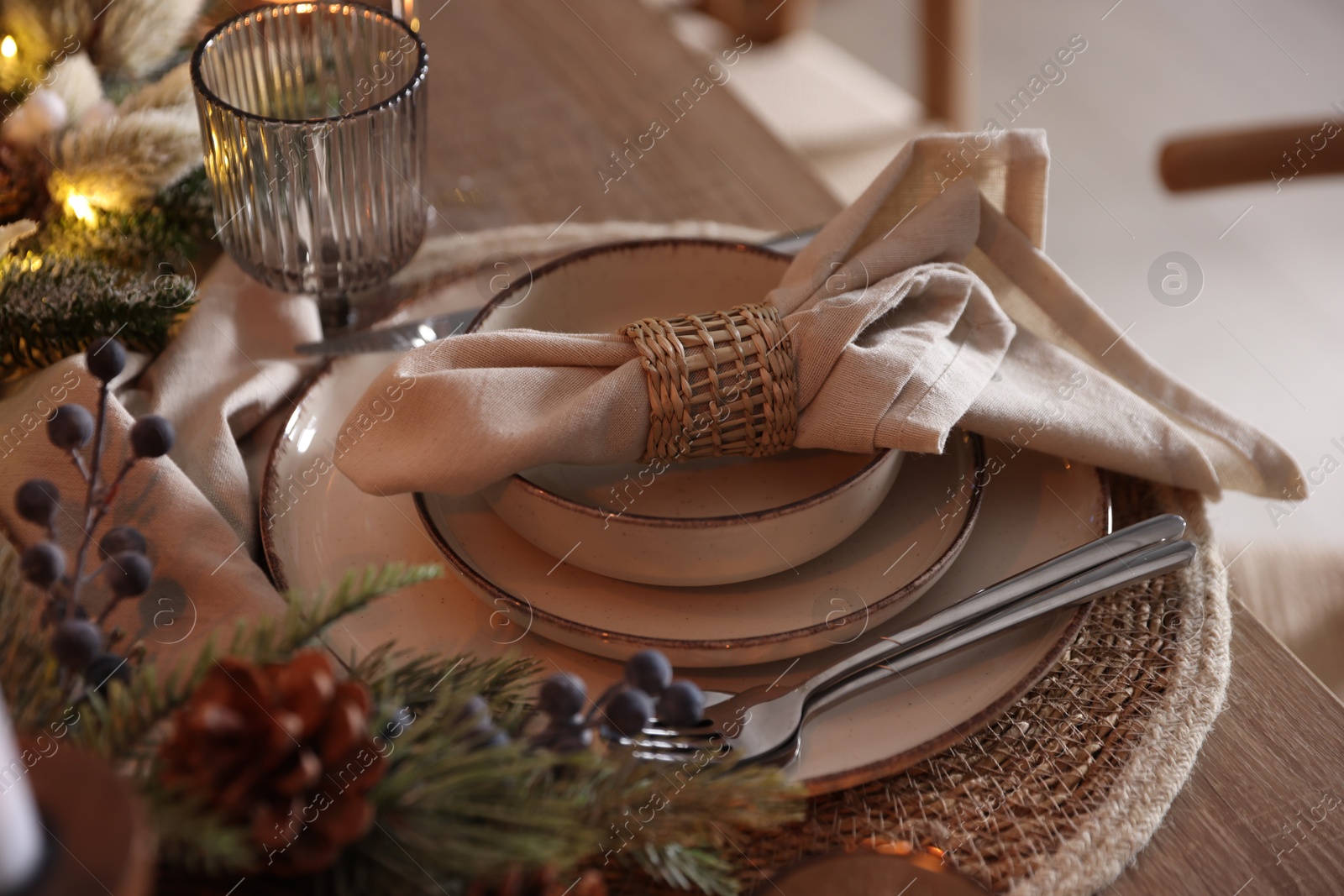 Photo of Christmas place setting with festive decor on wooden table in room, closeup