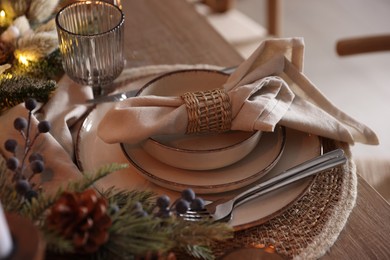 Photo of Christmas place setting with festive decor on wooden table in room, closeup