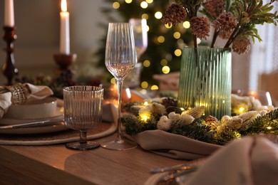 Photo of Christmas place setting with festive decor on wooden table in room, closeup