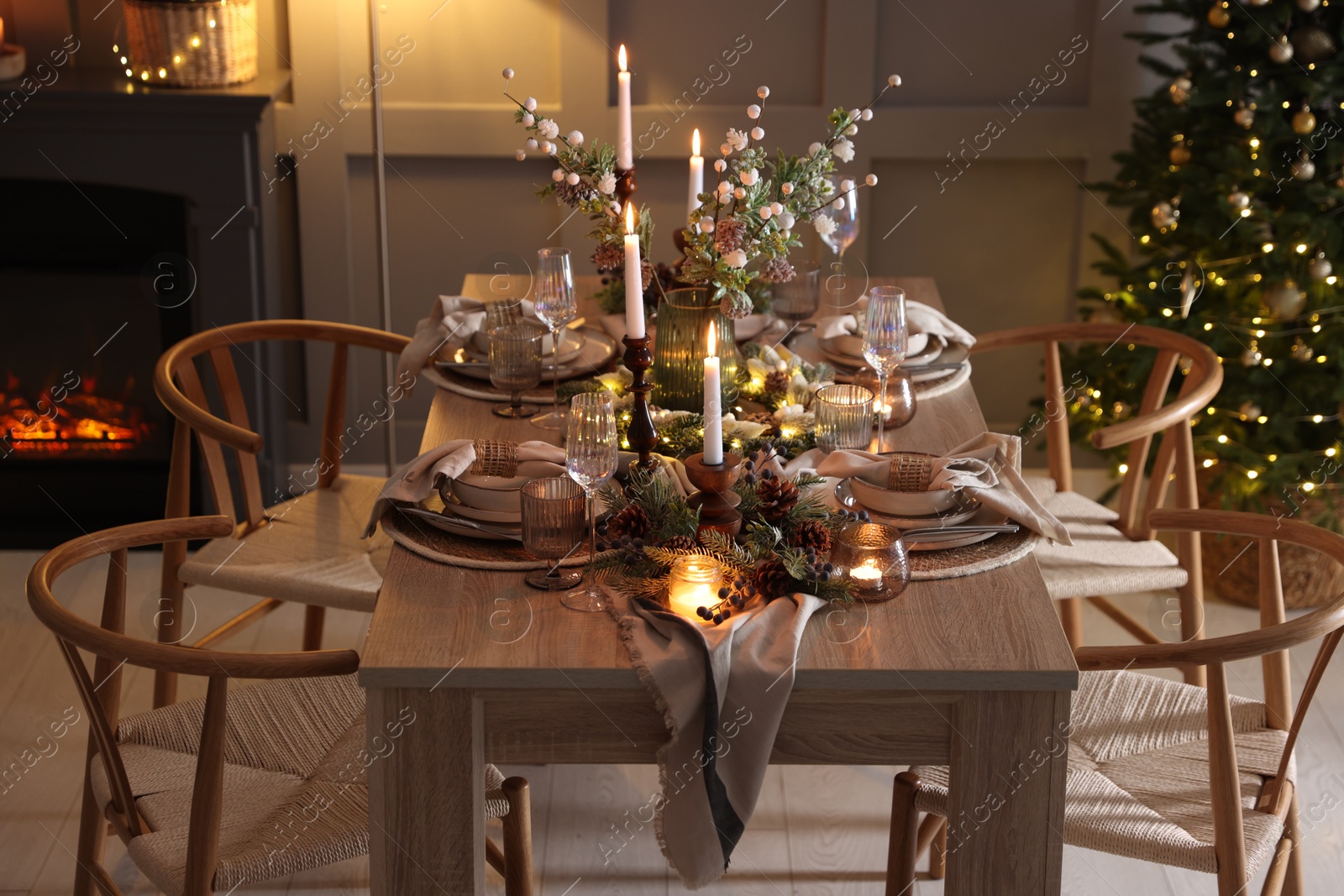 Photo of Christmas table setting with stylish dishware, glasses and burning candles in festive decorated room