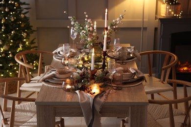 Photo of Christmas table setting with stylish dishware, glasses and burning candles in festive decorated room