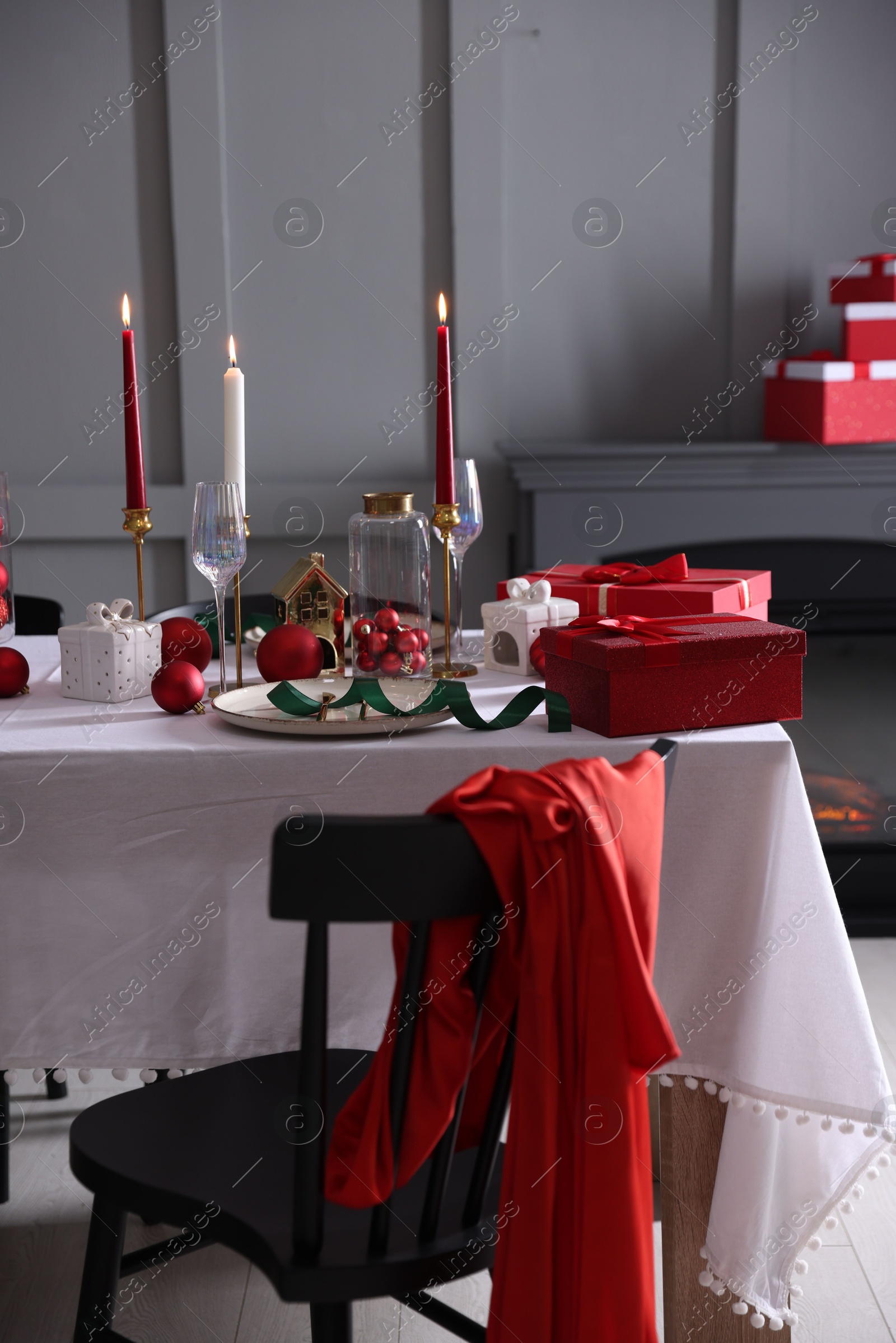 Photo of Christmas table setting with stylish dishware, glasses and burning candles in festive decorated room