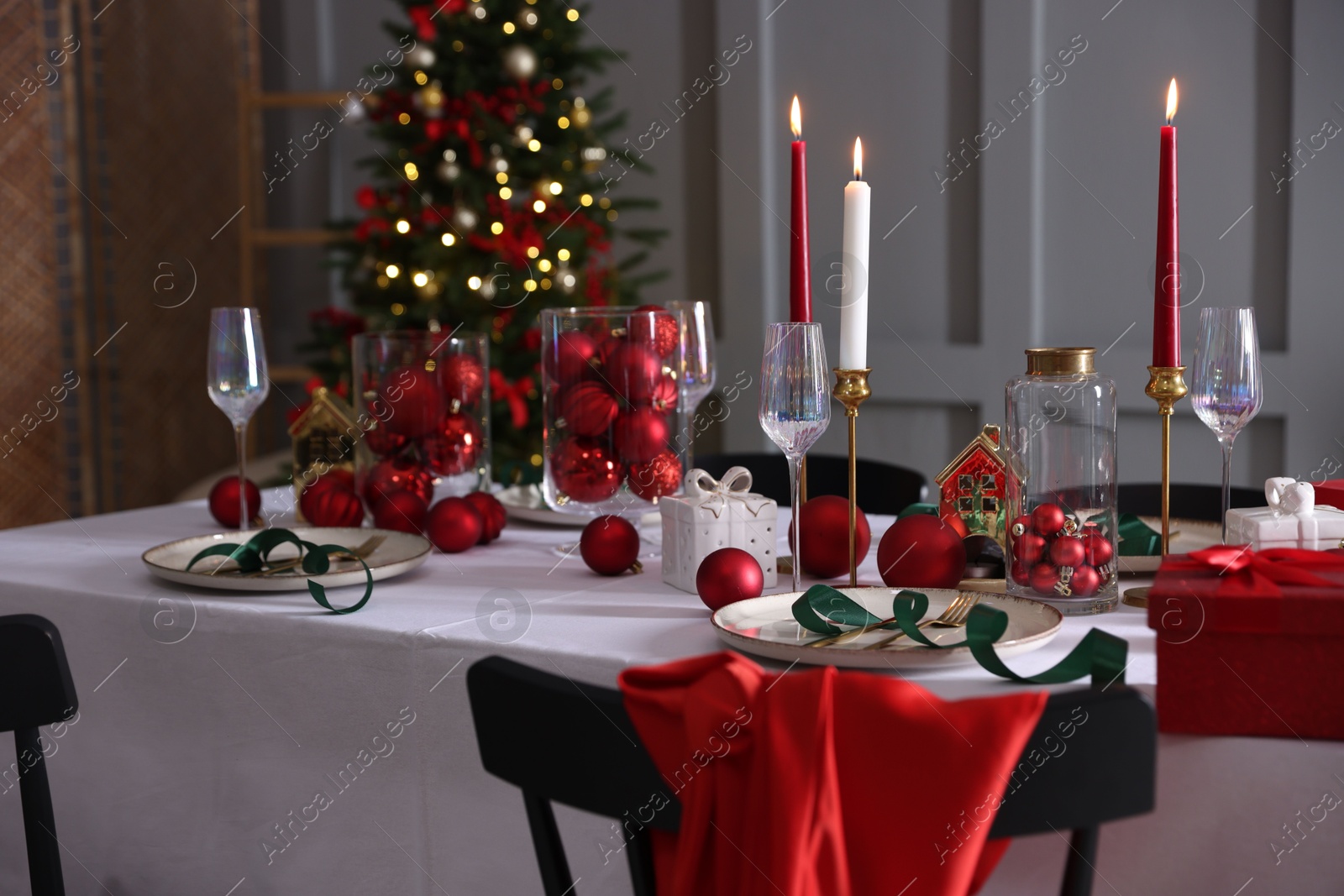 Photo of Christmas table setting with stylish dishware, glasses and burning candles in festive decorated room