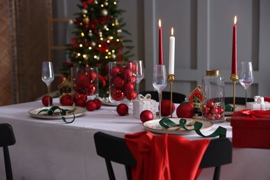 Photo of Christmas table setting with stylish dishware, glasses and burning candles in festive decorated room