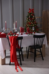 Photo of Christmas table setting with stylish dishware, glasses and burning candles in festive decorated room