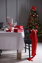 Photo of Christmas table setting with stylish dishware, glasses and burning candles in festive decorated room