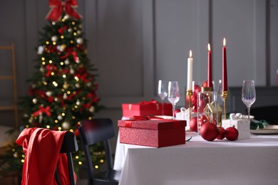 Photo of Christmas table setting with glasses and burning candles in festive decorated room