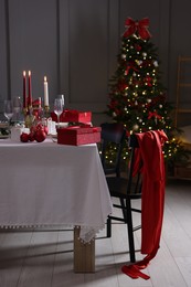 Photo of Christmas table setting with glasses and burning candles in festive decorated room