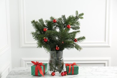 Photo of Beautiful decorated fir tree branches and Christmas gifts on table near white wall